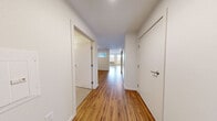 This efficiently designed single-floor unit offers a thoughtful layout that maximizes its compact footprint. Warm-toned hardwood flooring runs throughout, creating visual continuity across all areas of the space.

The combined kitchen and living area serves as the central hub of the unit. The kitchen is outfitted with rich dark-brown cabinetry extending to the upper walls, providing substantial storage. A full suite of stainless steel appliances — including a range, over-the-range microwave, dishwasher, and refrigerator — pairs with light-colored countertops and a white tile backsplash for a clean, modern aesthetic. A pass-through window connects the kitchen zone to an adjacent area, enhancing the sense of openness. The living area is brightened by two large windows offering outdoor views of a residential neighborhood and tree line, and is equipped with a wall-mounted HVAC unit.

The hallway connects the main living space to the bathroom and additional areas, including an in-unit stacked washer and dryer. The bathroom features a dark-brown vanity with a stone-patterned countertop, an undermount sink, a large mirror, and chrome fixtures, conveying a polished, contemporary finish throughout.