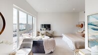 This contemporary studio is thoughtfully designed to maximize both function and style within a single-level open floor plan. Large floor-to-ceiling windows flood the living and sleeping areas with abundant natural light while framing impressive panoramic city views, creating a bright and airy atmosphere throughout. Light-toned tile flooring flows seamlessly across the main living space, reinforcing the clean, modern aesthetic.

The galley-style kitchen is outfitted with stainless steel appliances, including a full-size refrigerator, a range with a built-in microwave above, and ample cabinetry finished in warm wood tones paired with sleek white upper cabinets. A decorative hexagonal mosaic tile backsplash adds a refined visual detail, while white quartz countertops provide generous prep space.

The entry corridor offers additional storage and leads naturally into the open living and sleeping area, where vaulted ceilings enhance the sense of volume. A frosted glass sliding door provides a subtle architectural division within the space. The bathroom features a floating vanity, a framed mirror, and distinctive herringbone-patterned wood-look tile flooring, lending a warm yet contemporary finish. Together, the elements of this studio compose a cohesive, well-lit urban retreat.