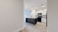 Located at 5025 Pilatus Wy in Mebane, NC, this single-floor, three-bedroom, two-bathroom home offers a well-designed layout with modern finishes throughout. The open-concept kitchen and living area serves as the heart of the home, featuring crisp white shaker cabinetry extending to the ceiling, a classic white subway tile backsplash, black appliances including a range, microwave, and refrigerator, and a striking dark-base kitchen island with a light countertop and built-in shelving, illuminated by pendant lighting overhead. Light wood-style luxury vinyl flooring runs throughout the main living and kitchen areas, lending a clean, cohesive aesthetic. The three bedrooms offer a comfortable retreat, with the primary bedroom providing a generous footprint. Secondary bedrooms are finished with plush carpeting and feature windows with blinds that invite natural light. The two bathrooms are finished with wood-style flooring, vanities with dark countertops, and tub-shower combinations. A dedicated laundry room with wire shelving and washer/dryer hookups adds everyday convenience. Crown molding and ceiling fans are present throughout, contributing to a polished, move-in-ready feel across this thoughtfully laid-out home.