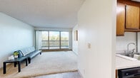 Located at 2101 Oakwood Rd in Ames, Iowa, this one-bedroom, one-bathroom unit offers a practical and comfortable single-floor layout. The living room is a bright, open space featuring plush carpeting and tile flooring that define separate zones, with a large sliding glass door that opens to a private balcony overlooking lush, tree-lined surroundings — filling the room with natural light and pleasant outdoor views. The galley-style kitchen is efficiently designed with warm oak cabinetry lining both walls, white appliances including a refrigerator, electric range, and dishwasher, a stainless steel sink, and durable tile flooring topped by a skylight panel for added brightness. The bedroom is a comfortable, carpeted retreat featuring a full-width sliding closet, a window for natural light, and a clean, neutral palette that provides a calm atmosphere. The full bathroom is outfitted with a wood-toned vanity with a wide countertop and single-basin sink, a large wall mirror, and a tub-shower combination with a decorative curtain. Throughout the unit, textured ceilings and neutral walls create a cohesive, understated aesthetic that is easy to personalize.