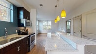 Located at 1055 Stratford Ave in Stratford, Connecticut, this well-appointed single-floor residence offers a thoughtfully designed layout filled with natural light throughout. The open-concept kitchen is a standout feature, boasting a generous granite-topped island illuminated by a trio of vibrant yellow pendant lights. Dark espresso cabinetry contrasts beautifully with the light stone countertops, while stainless steel appliances — including a range, microwave, and refrigerator — complete the space. Warm hardwood flooring extends from the kitchen into the spacious living area, which benefits from multiple large windows that frame views of the surrounding greenery, filling the room with an abundance of natural light. The bedrooms are finished with plush carpeting, neutral-toned walls, and windows that invite in natural light, creating calm and comfortable retreats. The bathrooms are clean and functional, featuring tile flooring, dark wood vanities with white countertops, and one bathroom equipped with a full soaking tub framed by large-format tile surround. Accessibility-conscious grab bars are also featured. A dedicated laundry area and ample closet space add to the practicality of this home. The overall ambiance is modern, bright, and welcoming, making it an inviting space in the heart of Stratford.