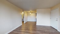 This single-floor unit in Denver, Colorado, near Fairmount Cemetery offers a straightforward, functional layout across several distinct living spaces. The open living area features wood-style hard flooring throughout, neutral-toned walls, and a textured ceiling. A ceiling fan provides overhead lighting and airflow, while a connected hallway leads to the remaining rooms, giving the space a cohesive flow.

The kitchen is equipped with dark espresso-toned cabinetry, light granite-style countertops, a stainless steel sink, a dishwasher, and a freestanding range with a ventilation hood. The matching wood-style flooring continues here, maintaining visual continuity with the living area. An additional open living or flex space features the same dark hardwood-style flooring and a bank of windows along one wall, allowing for ample natural light and outdoor views.

The bedroom is finished with wall-to-wall carpet and a single window that brings in natural light. The bathroom includes a full tub-shower combination with white tile surround and chrome fixtures. Throughout the unit, clean white baseboards and neutral wall tones create a simple, move-in-ready environment suited for everyday living.