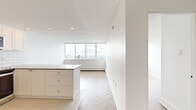 This thoughtfully designed one-bedroom, one-bathroom unit offers a clean, modern aesthetic throughout its efficiently laid-out single floor. The open-concept kitchen and living area serves as the heart of the unit, where a sleek peninsula with a dark countertop provides both prep space and a visual divider between the kitchen and living zones. The kitchen is outfitted with white shaker-style cabinetry, a classic white subway tile backsplash, stainless steel appliances including a range, microwave, and refrigerator, and a double undermount sink — delivering a polished, functional space. Light hardwood parquet flooring flows through the living and bedroom areas, adding warmth and texture. The living room benefits from expansive floor-to-ceiling windows that frame sweeping views of the city skyline, filling the space with abundant natural light. The bedroom is a comfortable size, featuring mirrored sliding closet doors and the same large windows offering impressive elevated city views. The bathroom is finished with full white subway tile walls, a stone-topped vanity with an undermount sink, and a tub-shower combination — maintaining the unit's consistent, clean design language throughout.