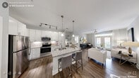 Located at 900 Doverside Dr in Apex, NC, this thoughtfully designed single-story home offers 2 bedrooms and 2 bathrooms across a comfortable, well-utilized floor plan. The open-concept kitchen and living area serves as the heart of the home, featuring crisp white shaker cabinets, granite countertops, stainless steel appliances, and a central island with bar seating illuminated by pendant lighting. Rich hardwood-style flooring flows throughout the main living spaces, adding warmth and continuity. The living room provides a bright, welcoming retreat with soft neutral tones and natural light. The primary bedroom is a generously sized sanctuary with plush carpet, a ceiling fan, and a large window that invites natural light. A spacious walk-in closet with wire shelving offers ample storage. The second bedroom is equally comfortable, maintaining the same neutral palette and cozy carpeting. Both bathrooms are finished with granite-topped vanities, white cabinetry, and clean tile flooring. A dedicated laundry room with full-size washer and dryer hookups adds everyday convenience. A welcoming hallway entry with hardwood-style flooring completes this polished, move-in-ready home.
