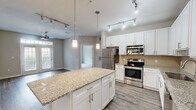 Located in Brookhaven, GA, this 2-bedroom, 2-bathroom residence offers a well-designed single-floor layout that balances comfort and functionality. The open-concept kitchen and living area serves as the heart of the home, featuring crisp white shaker cabinetry, granite countertops, a subway tile backsplash, and a full suite of stainless steel appliances including a refrigerator, range, microwave, and dishwasher. A large kitchen island with pendant lighting provides additional prep and dining space. The living area is bathed in natural light through French doors topped with transom windows, which open to the outdoors, and is complemented by a ceiling fan and durable hardwood-style flooring. Both bedrooms are carpeted and neutrally finished, offering a quiet retreat. The primary bedroom includes a walk-in closet. Both bathrooms are clean and functional, each featuring a tub-shower combination, white vanity with quartz-style countertops, and tile flooring. Additional spaces include two closets for ample storage. Track lighting throughout the common areas enhances the modern, well-lit ambiance of this thoughtfully appointed Brookhaven residence.