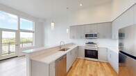 Located at 7460 SW Hermoso Way in Tigard, Oregon, this modern single-floor residence offers three bedrooms and two bathrooms within a thoughtfully designed, efficient floor plan. The open-concept kitchen and living area serves as the heart of the home, featuring sleek gray cabinetry extending to the ceiling, quartz countertops, a stainless steel appliance suite including a range, microwave, dishwasher, and refrigerator, and elegant pendant lighting over the sink peninsula. Light wood-tone flooring flows consistently throughout the space, enhancing the bright, clean aesthetic. The living area benefits from large windows and a glass door that open to a private balcony, offering sweeping outdoor views of the surrounding Tigard landscape. The primary bedroom is a comfortable, well-proportioned retreat with a dedicated window providing natural light. The two additional bedrooms are versatile, each featuring light flooring and windows. Both bathrooms are finished in a clean, contemporary style, with one featuring a full tub-shower combination. Hallways connect the rooms efficiently, and a closet adds practical storage. The consistently white walls and high ceilings throughout amplify the sense of openness, making this a bright and welcoming residence.