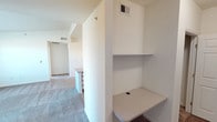 This single-floor unit offers a practical and functional layout designed to maximize usability throughout. The open-concept living area flows seamlessly toward the kitchen, where wood-trimmed cabinetry with white panel doors provides ample storage. Light-toned laminate countertops extend across the workspace, complemented by a double-basin stainless steel sink, an electric range, a refrigerator, and a dishwasher. Track lighting overhead adds focused illumination to the kitchen zone.

The living space features vaulted ceiling sections that lend a sense of openness, with neutral carpet underfoot and crisp white walls throughout. A built-in desk nook with a laminate work surface and an upper shelf offers a dedicated workspace, conveniently located near the hallway with a cable management cutout.

The bedrooms are carpeted and well-proportioned, each benefiting from large windows that invite natural light and provide open outdoor views of the surrounding landscape. The bathroom is equipped with a wide vanity featuring white cabinetry, a single sink with granite-toned countertop, a large mirror with Hollywood-style lighting, and tile flooring. The unit's neutral palette and consistent finishes create a clean, move-in ready environment throughout.