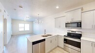 Located at 251 W 12th St in Ogden, Utah, this well-appointed one-bedroom, one-bathroom residence offers a thoughtfully designed single-floor layout with a clean, modern aesthetic. The open-concept kitchen and living area serves as the heart of the home, featuring light hardwood-style flooring, recessed lighting, and a contemporary pendant chandelier. The kitchen is outfitted with white shaker cabinetry, light quartz countertops, a peninsula with an integrated sink, and stainless steel appliances including a refrigerator, range, and built-in microwave. The living area benefits from abundant natural light through large windows that frame views of the surrounding neighborhood. The spacious primary bedroom is finished with plush carpeting and includes sliding glass doors that open to a private balcony, bringing in additional natural light and outdoor access. The full bathroom features a clean, all-white design with a single-sink vanity, ample drawer storage with brushed hardware, large-format tile flooring, and a full tub-shower combination. A dedicated in-unit laundry area houses a full-size washer and dryer with overhead shelving for added storage. A separate closet completes the functional layout of this bright and efficiently organized residence.