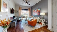 This single-floor residence presents a well-designed interior that balances bold color choices with contemporary finishes throughout. The living area serves as the centerpiece of the space, showcasing rich hardwood flooring, a ceiling fan, and a large sliding glass door that opens to an outdoor patio, flooding the room with natural light and views of the surroundings. A charcoal accent wall provides a striking backdrop for vibrant artwork, complementing the warm orange and neutral furnishings that define the room's energetic yet cohesive aesthetic. An additional workspace area is seamlessly integrated into the living space.

The kitchen is outfitted with dark espresso cabinetry, a light subway tile backsplash, white quartz countertops, a central island, and a full suite of stainless steel appliances, including a refrigerator, range, microwave, and dishwasher. Pendant lighting adds a polished finishing touch.

The bedroom features plush carpeting, a bold orange accent wall, and a large window dressed with layered curtains that invite natural light while maintaining privacy. The bathroom offers dark cabinetry paired with a dual-sink white vanity, a large mirror, and clean large-format tile flooring, conveying a sleek, spa-like quality.
