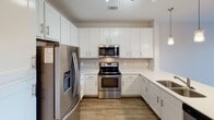 Located at 151 E Blount Ave in Knoxville, Tennessee, this well-appointed single-floor residence offers a thoughtfully designed open-concept layout. The kitchen serves as a centerpiece of the living space, boasting white shaker cabinetry with ample storage, a classic subway tile backsplash, and a full suite of stainless steel appliances including a French door refrigerator, electric range, and over-the-range microwave. A kitchen island with a double sink and pendant lighting above adds both functionality and style, flowing seamlessly into the living area. The living room features wood-style plank flooring, a ceiling fan, and a set of French doors that open to a private balcony, filling the space with natural light and offering pleasant outdoor views. The bedroom is generously sized, finished with plush carpet, a ceiling fan, and a large window that continues the theme of natural light throughout. The bathroom features a wide vanity with white cabinetry, a well-lit mirror, and a tub-shower combination. Directly accessible from the bathroom, a spacious walk-in closet with wire shelving provides excellent organizational capacity. Track lighting, recessed fixtures, and consistent wood-style flooring throughout the main areas complete the clean, contemporary aesthetic of this Knoxville residence.