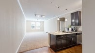 This single-floor residence offers a thoughtfully designed open-concept layout that seamlessly connects the kitchen and living area. The kitchen is a standout feature, showcasing rich dark espresso cabinetry, granite countertops, a peninsula island with pendant lighting, and a full suite of stainless steel appliances including a refrigerator, range, and microwave. Track lighting overhead provides excellent task illumination, while hardwood-style flooring anchors the kitchen space. Crown molding runs throughout, adding a refined architectural detail to the neutral, warm-toned walls.

The living area transitions smoothly from the kitchen, featuring plush carpeting, a ceiling fan, and a window that invites natural light. The bedrooms are generously proportioned, each finished with soft carpet, clean white baseboards, and windows dressed with blinds—one bedroom includes a ceiling fan for added comfort.

The bathroom is well-equipped with a tub and shower combination featuring white tile surround, dark wood vanity cabinetry with granite countertops, a large mirror, and hardwood-style flooring. Throughout the space, a consistent palette of warm beige tones and crisp white trim creates a cohesive, welcoming ambiance.