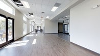 This two-floor clubhouse offers a well-appointed community space designed for both relaxation and socializing. The main level features a expansive open-plan interior with neutral-toned, wood-look flooring and a drop ceiling fitted with recessed fluorescent lighting. Large windows line the perimeter, drawing in generous natural light and creating a bright, welcoming atmosphere. The clean white walls and open layout provide a versatile setting suitable for gatherings and events, with a dining area visible toward the rear of the space. Double glass entry doors provide an elegant point of arrival.

The second floor opens onto a spacious rooftop terrace finished with large-format porcelain tile. This outdoor space offers panoramic waterfront views, with a marina and cityscape visible in the distance. The terrace is equipped with stylish outdoor seating arrangements, including cushioned lounge chairs, side tables, and shaded umbrella seating, making it ideal for enjoying the scenery. A metal railing encloses the perimeter for safety.

Complementing the building is a generously sized outdoor swimming pool, surrounded by a paved deck with lounge chairs and framed by mature trees, offering a serene retreat in a park-like setting.