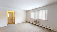 This single-floor residential unit offers a straightforward, functional layout designed for comfortable everyday living. The living area is generously proportioned, featuring neutral wall-to-wall carpeting and crisp white walls that create a bright, open atmosphere. A large window dressed with vertical blinds allows natural light to filter in, while a baseboard heating system and wall-mounted air conditioning unit ensure year-round climate control.

The bedroom is well-sized with soft carpeting underfoot, a window overlooking the outdoors, and two full-width closets with bi-fold doors, providing ample storage. A second carpeted room with a ceiling light fixture and its own window offers flexible use as an additional bedroom or den.

The galley-style kitchen is efficiently arranged with warm wood-toned cabinetry, dark granite-look countertops, a stainless steel sink, a coil-top range, and a full-size refrigerator. Light ceramic tile flooring and a pantry closet add to the kitchen's practicality.

The full bathroom includes a tub-shower combination with tile surround, a wood-vanity with dark countertop, a toilet, and small-format tile flooring. Overall, the unit presents a clean, move-in ready environment with consistent finishes throughout.