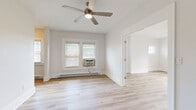 Located at 1416 Lewis Drive in Lakewood, Ohio, this thoughtfully renovated 2-bedroom, 1-bathroom unit offers a clean, modern aesthetic across a well-organized single floor. Light wood plank flooring runs consistently throughout every room, creating a cohesive and airy feel. The living room is bright and open, benefiting from multiple windows dressed with white blinds and a ceiling fan overhead, while baseboard heating ensures year-round comfort. A narrow hallway connects the main living areas, featuring an electrical panel and a smoke detector, providing a practical transition between spaces. The kitchen is a standout feature, outfitted with floor-to-ceiling walnut-toned cabinetry, crisp white quartz countertops, a stainless steel sink, and a stainless steel range — offering both ample storage and functional workspace. The primary bedroom is generously sized, accommodating a ceiling fan, multiple windows for natural light, and a wall-mounted air conditioning unit. The second bedroom is more compact, featuring a window with outdoor views and access to the hallway. The bathroom is finished with contemporary wood-grain vanity cabinetry, a white countertop, a mirror, and a combined tub-shower with a window providing natural ventilation. Clean white walls and bright, neutral tones throughout contribute to the overall fresh and move-in-ready atmosphere of this Lakewood residence.