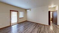 This 1-bedroom, 1-bathroom residence in Edgewood, WA offers a practical and comfortable single-floor layout. The kitchen is a functional highlight, featuring rich warm-toned cabinetry, white countertops, stainless steel appliances including a French door refrigerator, electric range, and built-in microwave, complemented by a peninsula that provides additional counter space and separates the kitchen from the living area. The flooring throughout the kitchen and living spaces consists of durable wood-look planks in a neutral gray tone, lending a clean and modern feel. The living area is bright and open, benefiting from natural light through a large window fitted with blinds, and is equipped with a wall-mounted mini-split HVAC unit for year-round comfort. The bedroom is generously proportioned, finished with soft wall-to-wall carpeting, a closet with a paneled door, and a window that invites natural light. The bathroom is cleanly designed with a combination tub and shower, a single-sink vanity with warm wood cabinetry and white countertop, a large mirror, and tile flooring. Warm wood trim accents and neutral wall tones throughout the space create a cohesive and inviting atmosphere.