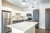 This modern single-story, two-bedroom, one-bathroom home in Fitchburg, Wisconsin offers a thoughtfully designed layout with clean, contemporary finishes throughout. The kitchen serves as a central highlight, featuring a large white-quartz island, a two-tone cabinet scheme pairing crisp white upper cabinets with sleek gray lower cabinets, a subway tile backsplash, and a full suite of stainless steel appliances including a refrigerator, range, microwave, and dishwasher. Globe pendant lights hang above the island, adding a modern touch. The kitchen flows naturally toward a living area with sliding glass doors that invite natural light and outdoor views. Both bedrooms are well-proportioned and bright, each benefiting from large windows with blinds and ceiling fans for year-round comfort. Neutral warm-toned walls complement the light flooring found throughout the home. The bathroom is cleanly appointed with gray cabinetry, a white quartz countertop, an undermount sink with brushed nickel fixtures, a large mirror, and ample towel bar storage. Additional conveniences include a dedicated laundry room, two hallways for smooth circulation, and dual entrances. The overall ambiance is fresh, minimalist, and move-in ready.