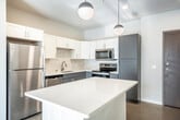 This modern single-story, two-bedroom, one-bathroom home in Fitchburg, Wisconsin offers a thoughtfully designed layout with clean, contemporary finishes throughout. The kitchen serves as a central highlight, featuring a large white-quartz island, a two-tone cabinet scheme pairing crisp white upper cabinets with sleek gray lower cabinets, a subway tile backsplash, and a full suite of stainless steel appliances including a refrigerator, range, microwave, and dishwasher. Globe pendant lights hang above the island, adding a modern touch. The kitchen flows naturally toward a living area with sliding glass doors that invite natural light and outdoor views. Both bedrooms are well-proportioned and bright, each benefiting from large windows with blinds and ceiling fans for year-round comfort. Neutral warm-toned walls complement the light flooring found throughout the home. The bathroom is cleanly appointed with gray cabinetry, a white quartz countertop, an undermount sink with brushed nickel fixtures, a large mirror, and ample towel bar storage. Additional conveniences include a dedicated laundry room, two hallways for smooth circulation, and dual entrances. The overall ambiance is fresh, minimalist, and move-in ready.
