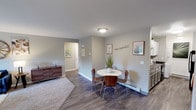 Located at 2600 Raintree Dr in Fort Collins, Colorado, this single-floor residence offers a well-designed layout with a comfortable, functional interior throughout. The living room is a welcoming space featuring large multi-pane windows that flood the room with natural light and frame views of the surrounding greenery. Durable wood-style flooring flows through the dining and kitchen areas, while plush carpet adds warmth to the living and bedroom spaces. The dining area sits adjacent to the kitchen and offers a relaxed setting, complete with baseboard heating. The kitchen is outfitted with dark granite-style countertops, white cabinetry, a stainless steel sink, and black appliances. A dedicated in-unit laundry area with a stacked washer and dryer is conveniently located nearby. Both bedrooms are carpeted, feature ceiling fans, and receive natural light through standard windows. The primary bedroom is accompanied by a private vanity area with dark granite counters and ample cabinet storage. A full bathroom with a walk-in shower, grab bars, and wood-style flooring serves the rest of the unit. A walk-in closet provides generous storage. The overall aesthetic is clean and neutral, creating a move-in ready environment in a well-situated Fort Collins location.