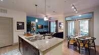This single-floor residence offers a thoughtfully designed open-concept layout that seamlessly connects the kitchen, dining, and living areas. The kitchen is equipped with stainless steel appliances, granite countertops, dark cabinetry, and a central island with a double sink, providing ample workspace and storage. Track lighting overhead enhances the functional character of the space. The adjoining dining area features a bold teal accent wall, a glass-paneled door opening to the outdoors, and room for a comfortable dining set. The living room continues the teal color scheme and is anchored by light hardwood-style flooring, a ceiling fan, and a large window that invites natural light. An arched passageway adds an architectural touch connecting the main living areas. Both bedrooms are carpeted and feature multiple windows with outdoor views, ceiling fans, and generous space for furnishings. The full bathroom includes a tiled shower-tub combination, dark vanity cabinetry, and stone-topped counters. A dedicated in-unit laundry room with side-by-side washer and dryer and built-in shelving adds everyday convenience. The consistent use of light flooring, neutral walls, and vibrant accent tones throughout creates a cohesive and modern aesthetic.