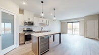 Located at 6470 37th Ave NW in Rochester, MN, this well-appointed single-floor home offers three bedrooms, two bathrooms, and a thoughtfully designed layout. The open-concept kitchen and living area serves as the heart of the home, featuring white shaker-style cabinetry, stainless steel appliances, a subway tile backsplash, and a central island with a quartz countertop and a built-in beverage cooler. Pendant lighting with glass fixtures adds a modern touch, while light hardwood flooring flows seamlessly throughout the main living and kitchen areas. A sliding glass door in the living room opens to a private balcony, filling the space with natural light and outdoor views. The bedrooms are carpeted and neutral-toned, offering a calm and comfortable atmosphere. The generously sized primary bedroom includes a walk-in closet with wire shelving for ample storage. The bathrooms feature warm wood-toned vanities with white countertops and durable luxury vinyl plank flooring. Additional bedrooms display a mix of neutral warm and cool tones, providing versatile spaces suitable for sleeping, working, or other uses. Clean lines, neutral color palettes, and contemporary finishes throughout give this home a cohesive, modern aesthetic.