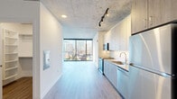 Located in Chicago's vibrant River North neighborhood, this studio offers a thoughtfully designed open-concept layout that combines the kitchen and living area into one cohesive, light-filled space. Exposed concrete ceilings lend an industrial character throughout, complemented by light wood-tone flooring that runs seamlessly from room to room.

The kitchen is fully equipped with stainless steel appliances, including a range, built-in microwave, dishwasher, and refrigerator. Two-tone cabinetry — featuring white upper cabinets and wood-finish lower cabinets — pairs with a white tile backsplash and a clean-lined countertop with an undermount sink. Track lighting accents the kitchen and adds functional illumination.

The living area is anchored by expansive floor-to-ceiling windows that frame striking views of the Chicago skyline, flooding the space with natural light. The open layout provides flexibility for various furniture arrangements.

The bathroom features a generous vanity with a quartz countertop, an undermount sink, dark wood cabinetry with matte black hardware, and a backlit mirror that adds a contemporary touch. A closet off the main hallway houses a stacked washer and dryer, offering convenient in-unit laundry. The combination of industrial design elements and modern finishes gives this studio a polished, urban aesthetic.