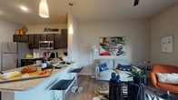 This single-story, one-bedroom, one-bathroom residence offers a thoughtfully designed open-concept layout that maximizes its compact footprint. The kitchen is a standout feature, showcasing dark espresso cabinetry, stainless steel appliances including a refrigerator, microwave, and range, complemented by granite countertops and a white subway tile backsplash. A peninsula with bar seating and pendant lighting above serves as both a functional prep area and a casual dining space, seamlessly connecting the kitchen to the living area. Wood-style plank flooring runs throughout the unit, lending warmth and visual continuity across the space. The living area is comfortably sized, receiving natural light from nearby windows. The bedroom accommodates a full-sized bed and features a window with blinds and curtains, a ceiling fan, and access to a walk-in closet. The bathroom continues the cohesive design with matching dark cabinetry, a granite-topped vanity, and wood-style flooring. Neutral wall tones throughout contribute to a clean, modern aesthetic, while recessed and pendant lighting ensure well-lit spaces. The overall ambiance is contemporary, practical, and efficiently arranged for comfortable single-occupant living.