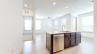 This single-story unit showcases a clean, contemporary design with a bright, open layout. The kitchen serves as the central highlight, featuring a large island with granite countertops and an undermount sink, rich dark-toned cabinetry extending to the upper walls, and a full suite of stainless steel appliances including a refrigerator with ice maker, electric range, microwave, and dishwasher. Recessed lighting and multiple windows with horizontal blinds fill the space with natural light.

Light wood-style plank flooring flows throughout the main living and kitchen areas, creating a cohesive, airy feel. Ceiling fans are present in the open living areas, adding both function and a finishing detail to the interiors. The bedrooms are carpeted for added comfort and include windows that bring in natural light. One bedroom features a walk-in closet with built-in shelving and hanging rods, providing ample storage.

The bathroom includes a vanity with granite countertops and dark cabinetry, a tub-shower combination with white tile surround, and light wood-style flooring consistent with the rest of the unit. Throughout, crisp white walls and panel-style interior doors contribute to the space's clean, modern aesthetic.