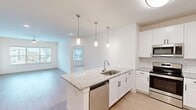 This single-floor residence in Athens, Alabama offers a thoughtfully designed layout across two bedrooms and two bathrooms. The open-concept kitchen and living area serves as the heart of the home, anchored by a central island with granite countertops, an undermount sink, and pendant lighting overhead. White shaker cabinetry, subway tile backsplash, and a full suite of stainless steel appliances — including a refrigerator, range, microwave, and dishwasher — complete the kitchen. Light wood-style flooring flows throughout the main living areas, contributing to a bright, cohesive aesthetic. The living room receives generous natural light through a wide bank of windows fitted with blinds, and a ceiling fan adds practical comfort. Both bedrooms feature neutral carpet and crisp white walls. The primary bathroom is well-appointed with a dual-sink granite vanity, white cabinetry, a glass-enclosed shower, and access to a walk-in closet. The second bathroom mirrors the clean design with a granite vanity and a tiled tub-shower combination. Throughout, the consistent use of white finishes and granite surfaces creates a modern, unified atmosphere.