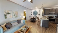 This thoughtfully designed 2-bedroom, 2-bathroom single-floor residence offers a comfortable and functional layout across a well-proportioned floor plan. The open-concept living and dining area is anchored by warm hardwood-style flooring, soft neutral wall tones, and a ceiling fan overhead. The living room provides an inviting atmosphere with natural light filtering through large windows dressed with decorative curtains. The adjacent dining space features a charming round table beneath a statement oversized wall clock, adding character to the area. The kitchen is a standout feature, outfitted with dark gray shaker-style cabinetry, granite countertops, a classic white subway tile backsplash, stainless steel appliances, and a built-in wine rack. A convenient in-unit laundry closet with a full-size washer and dryer is located just off the kitchen. Both bedrooms are comfortably sized with soft carpeting and warm lighting. The primary bedroom features a bold accent wall and ample closet space, while the second bedroom offers a cozy, neutral aesthetic. Each of the two bathrooms includes a tub-shower combination, tile flooring, and granite vanity tops, maintaining a consistent level of finish throughout the home.