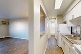 Located at 10623 E Exposition Ave in Aurora, CO, this one-bedroom, one-bathroom unit offers a practical and functional single-floor layout. The living room is an open, well-proportioned space featuring wood-style plank flooring, neutral gray walls, a wall-mounted AC unit, and a baseboard heating system. A large window allows natural light to fill the room while providing views of the surrounding area. A pass-through counter connects the living area to the galley-style kitchen, which is outfitted with white cabinetry, white appliances including a coil-top range and refrigerator, a sink, and a skylight-style ceiling fixture that brightens the narrow workspace. A hallway connects the main living areas to the private spaces, leading to the generously sized bedroom. The bedroom features soft carpet flooring, neutral tones, and a double-door closet offering ample storage. A baseboard heater and window round out the room. The bathroom includes a full-size soaking tub with tile surround, a window for natural ventilation, and clean white finishes throughout. The overall aesthetic is clean, neutral, and move-in ready.
