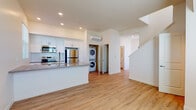 This modern two-story residence at 310-340 Palm Ave in National City, California, offers a clean, contemporary design with thoughtful details throughout. The main level features an open-concept living and kitchen area bathed in natural light, with large windows framing neighborhood views. Light wood-tone flooring flows seamlessly across both floors, creating a warm and cohesive aesthetic.

The kitchen is well-appointed with white shaker cabinetry, grey countertops, a classic subway tile backsplash, and a full suite of stainless steel appliances, including an electric range, over-the-range microwave, and refrigerator. A peninsula with a built-in sink adds functional counter space while connecting the kitchen to the living area. The main level also features a dedicated in-unit laundry closet with a stacked washer and dryer.

A staircase leads to the upper level, where multiple bright bedrooms offer comfortable proportions, natural light from windows with blinds, and wall-mounted mini-split HVAC units for individual climate control. The bathrooms are finished in a clean, modern style with white vanities featuring black hardware, large mirrors, and tile surrounds. One bathroom includes a tub-shower combination, while another features a standalone shower. The overall design is fresh, functional, and move-in ready.