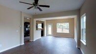 This two-story home offers a thoughtfully designed layout that balances open communal spaces with functional living areas. The main level showcases an open-concept floor plan where the living area flows seamlessly into the dining space and kitchen. Dark hardwood-style flooring runs throughout, providing a rich contrast against the warm, neutral-toned walls and crisp white trim and baseboards.

The living area is equipped with a ceiling fan, adding both practicality and a finishing touch to the space. Adjacent to it, a defined dining area is illuminated by an elegant chandelier and benefits from abundant natural light streaming through a set of large windows, which also offer views of the surrounding greenery outdoors.

The kitchen is visible from the main living area and features dark cabinetry, black appliances including a refrigerator and range, and a raised breakfast bar that serves as a natural divider between the kitchen and the adjoining spaces. The layout allows for easy interaction between the kitchen and living areas, making it well-suited for entertaining.

The home extends across two floors, offering additional living space above the main level. Overall, the interior presents a clean, move-in-ready aesthetic with a cohesive color palette and durable, low-maintenance finishes throughout.