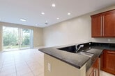 Located at 5146 NW 30th Lane in Fort Lauderdale, Florida, this two-story residence offers a well-organized layout across both levels. The main floor is anchored by a kitchen designed for functionality and style, featuring rich cherry wood cabinetry, dark granite countertops, a peninsula with an undermount sink, and a full suite of stainless steel appliances including a refrigerator, range, microwave, and dishwasher. Recessed lighting illuminates the space, which opens toward a generously sized living area finished with light-toned ceramic tile flooring. The open sightlines between the kitchen and living spaces create a cohesive, practical flow throughout the main level. A staircase with a wood railing and wrought iron balusters connects to the upper floor, where carpeted bedrooms provide a comfortable, quieter retreat. Each bedroom is finished with warm neutral tones and benefits from natural light through windows with views of the surrounding neighborhood. Bathrooms are finished with tile throughout, offering both a tub-shower combination and a separate glass-enclosed shower. The consistent use of neutral tones and tile flooring on the main level gives the home a clean, cohesive aesthetic throughout.