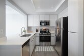 Located at 2596 Associated Rd in Fullerton, California, this single-floor residence offers a well-organized layout designed for comfortable everyday living. The open living area is finished with light wood-style flooring and neutral gray walls, creating a bright and airy atmosphere. A ceiling fan adds both function and style, while a pass-through opening connects the living space seamlessly to the kitchen. Large sliding glass doors lead to a private balcony, where views of mature palm trees and the surrounding neighborhood provide a distinctly Southern California ambiance. Transom windows above the doors allow additional natural light to fill the room.

The kitchen is thoughtfully appointed with white cabinetry, white quartz countertops, and a full suite of stainless steel appliances including a gas range, over-the-range microwave, dishwasher, and refrigerator. Recessed lighting illuminates a tray ceiling detail overhead, enhancing the clean, modern aesthetic.

The bedrooms are carpeted for warmth and comfort, each featuring mirrored sliding closet doors that add depth and reflect light throughout the rooms. Windows with blinds provide natural light and privacy. The bathroom is finished with wood-style flooring, a modern vanity with a white countertop, and a full shower-tub combination.