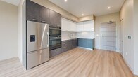 This modern 2-bedroom, 2-bathroom residence in Roseville, CA is thoughtfully designed with clean lines and contemporary finishes throughout. Light hardwood-style flooring flows seamlessly across the entire single-level layout, creating a cohesive and airy aesthetic.

The open-concept kitchen and living area serves as the heart of the home. The kitchen is outfitted with two-tone cabinetry — dark charcoal lower cabinets paired with crisp white upper cabinets — complemented by light countertops, a stainless steel sink, a built-in double oven, and a full-size stainless steel refrigerator with an ice and water dispenser. Recessed lighting illuminates the space efficiently.

The living area is bathed in natural light through expansive floor-to-ceiling windows and a glass door that opens to an outdoor view of the surrounding streetscape and tree canopy, enhancing the sense of openness.

Both bedrooms continue the light flooring and neutral warm-toned walls, with large windows offering ample natural light and outdoor views. The primary bedroom features oversized glazed panels framing a bright urban outlook.

Each bathroom is finished with light tile flooring and features a full tub-shower combination with a curved curtain rod. One bathroom includes a vanity with a light countertop and contemporary cabinetry. Clean hallways with recessed lighting connect the rooms, and a dedicated closet provides additional storage.