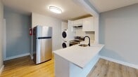 Located at 319 Columbia Ave in Stratford, NJ, this thoughtfully renovated single-floor unit showcases clean, modern finishes throughout. Light wood luxury vinyl flooring runs continuously across the open layout, complementing the soft gray-blue walls and crisp white trim that create a calm, cohesive aesthetic.

The open-concept living area is bright and spacious, illuminated by recessed lighting and natural light from well-placed windows that offer views of surrounding greenery. A wrought-iron railing accents the staircase entry, adding a contemporary architectural detail to the space.

The kitchen is efficiently designed with white shaker cabinetry, a sleek white quartz peninsula countertop, a stainless steel refrigerator, an electric range, and a matte black faucet over a stainless sink. A stacked washer and dryer unit is conveniently integrated within the kitchen area, providing in-unit laundry without sacrificing layout flow.

The bedrooms are comfortably sized, each featuring the same warm wood flooring, soft wall tones, and windows with natural views. Wall-unit air conditioners and baseboard heating ensure year-round climate comfort.

The bathroom is finished in a clean, all-white palette with large-format marble-look tile surrounding the soaking tub and shower, a white vanity with brushed nickel hardware, and tile flooring — delivering a crisp, spa-like feel.