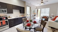 This well-appointed single-story residence offers a thoughtfully designed open-concept layout that seamlessly connects the kitchen, dining, and living areas. The kitchen is a standout feature, outfitted with dark espresso cabinetry extending to the ceiling, stainless steel appliances including a refrigerator, range, microwave, and dishwasher, and bright white countertops that contrast sharply against the dark finishes. Light wood-style flooring runs throughout the main living areas, enhancing the clean, contemporary aesthetic.

The dining area accommodates a glass-top table situated adjacent to the kitchen, while the living room benefits from generous natural light streaming through large windows and a sliding glass door that opens to an outdoor balcony. Ceiling fans are present in both the living room and bedrooms, contributing to the unit's comfortable atmosphere.

Both bedrooms are carpeted and well-sized, each featuring ceiling fans and windows with views of surrounding greenery. The primary bathroom includes a dual-sink vanity with dark cabinetry and a large mirror, while a second bathroom provides a single-sink vanity with matching finishes. Neutral wall tones and consistent design elements throughout create a cohesive, modern living environment.