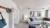 Located in Towson, MD, this 2-bedroom, 1-bathroom residence offers a well-organized single-floor layout that balances comfort and functionality. The living room serves as the heart of the home, featuring plush wall-to-wall carpeting, large windows that fill the space with natural light, and a clean white palette that creates a bright, airy atmosphere. The adjacent dining area continues the modern aesthetic, highlighted by a tray ceiling, a large window with natural light, and elegant black-framed glass panel accents that visually connect to the kitchen. The kitchen is equipped with rich cherry wood cabinetry, light stone countertops, black appliances including a range, dishwasher, and refrigerator, and warm hardwood flooring that adds a classic touch. Both bedrooms are carpeted and well-lit, with the primary bedroom offering a comfortable sense of space and a window with outdoor views. The full bathroom features white subway tile walls, a wood-toned vanity with a white countertop, and a bright window for natural ventilation. Two hallways provide seamless connectivity throughout the unit. The overall ambiance is modern and inviting, with a neutral color scheme that lends itself to a variety of interior styles.