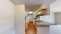 This single-floor unit offers a practical and well-organized layout designed for comfortable everyday living. The galley-style kitchen is efficiently arranged with appliances and cabinetry lining both walls, providing ample storage through cream-colored upper and lower cabinets. The kitchen features a double sink, electric range, refrigerator, and dishwasher, all finished in white, with warm wood-look flooring running the length of the space. A pass-through counter connects the kitchen to the main living area, creating an open, connected feel between the two spaces.

The living area is generously sized, featuring plush carpeting and a sliding glass door that opens to a private outdoor area, allowing natural light to filter in. A ceiling fan overhead adds to the comfort of the room. The adjoining area is open and versatile, suited for dining or additional living use.

The bedrooms are carpeted and bright, each equipped with ceiling fans and windows fitted with blinds that provide both privacy and natural light. The bathroom includes an extended countertop vanity with a wide mirror and bright overhead lighting, offering notable counter space for storage and daily use. Throughout, the unit features neutral wall tones and a textured ceiling, contributing to a clean, understated aesthetic.