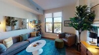 Located in Washington, DC's dynamic H Street NE corridor, this single-floor residence combines contemporary finishes with a warm, curated aesthetic. The living area serves as the heart of the home, featuring rich hardwood floors, a large window with views of the tree-lined street below, and thoughtfully arranged furnishings including a plush sofa, marble-top coffee table, and a bold teal area rug. Industrial-style open shelving and Edison bulb wall sconces flanking an art-adorned wall add character and depth to the space. The galley kitchen is efficiently designed with crisp white cabinetry, dark stone countertops, stainless steel appliances, and a soft blue subway tile backsplash — balancing form and function in a compact, well-organized layout. Warm hardwood flooring continues throughout, tying the spaces together cohesively. The bedroom offers a tranquil retreat with neutral tones, clean-lined white doors, and understated decor that promotes restful comfort. The bathroom is finished with large-format grey floor tiles, a sleek floating vanity with dark countertop, and clean white walls, delivering a modern, spa-like simplicity. Throughout the residence, an eclectic yet cohesive art collection and natural light contribute to an inviting and lived-in atmosphere.