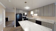 Located at 3278 Colony Ct in Greenville, NC, this two-floor home offers a thoughtfully updated interior with consistent finishes throughout. The kitchen is a standout feature, showcasing striking marble-look quartz countertops, grey shaker-style cabinetry, and pendant lighting above a central island. Black appliances — including a refrigerator, electric range, over-the-range microwave, and dishwasher — provide a bold contrast against the light countertops and cabinetry. Wood-look luxury vinyl plank flooring runs throughout the main living areas and bedrooms, adding warmth and continuity. The living area features crown molding and chair rail detailing, lending a classic, polished character to the space. Bedrooms are well-proportioned, with ceiling fans, natural light from windows with blinds, and generous closet space including built-in shelving. The bathrooms are clean and functional, featuring tub-shower combinations with chrome fixtures, and one bathroom showcases a grey vanity with a framed mirror and tri-light fixture above. Textured ceilings are present throughout. The overall palette of warm beige tones, white trim, and grey accents creates a cohesive and neutral aesthetic suitable for a variety of interior styles.