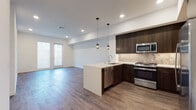 Located at 6532 Variel Ave in the Canoga Park neighborhood of Los Angeles, this single-floor unit presents a thoughtfully designed contemporary interior. The open-concept layout seamlessly connects the kitchen and living area, anchored by warm wood-look flooring that flows throughout the main living spaces. The kitchen is a standout feature, showcasing rich dark-wood cabinetry, a marble-style tile backsplash, and a full suite of stainless steel appliances including a gas range, built-in microwave, dishwasher, and French door refrigerator. A peninsula with a white countertop and undermount sink provides additional prep space and casual seating, while dual pendant lights add a refined touch overhead. Recessed lighting illuminates the open living area, which benefits from natural light through large windows and a glass-paneled door. The bedroom features plush carpeting and a bright window with blinds, offering a comfortable, quiet retreat. The bathrooms are finished in clean white tile, with one featuring a soaking tub and shower combination and another equipped with a glass-enclosed walk-in shower. Built-in shelving provides practical storage. The entry area includes a louvered closet door, completing this well-appointed modern space.
