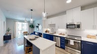 Located at 1909 Alexander Ave in Austin, TX, this well-designed one-bedroom, one-bathroom residence offers a thoughtfully arranged open-concept floor plan with light wood flooring throughout. The kitchen is a standout feature, showcasing bold navy lower cabinetry paired with crisp white upper cabinets, a herringbone tile backsplash, quartz countertops, stainless steel appliances, and a kitchen island with seating for two — illuminated by modern glass pendant lights. The open layout flows seamlessly into the living room, where a ceiling fan, large sliding glass doors, and access to a private balcony invite natural light and urban views. The bedroom is a comfortable retreat, complete with a ceiling fan, a large window overlooking the cityscape, and ample closet space. The bathroom features a clean, contemporary design with a white floating vanity, quartz countertop, black hardware accents, an LED-backlit mirror, and a full tub-shower combination with subway tile surround. Throughout the residence, a neutral color palette with light walls and warm wood-toned flooring creates a bright and cohesive ambiance well-suited to Austin's vibrant East Side neighborhood.