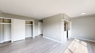 This single-floor unit presents a clean, modern aesthetic throughout, anchored by light wood-style luxury vinyl flooring and soft neutral grey walls that create a cohesive, contemporary feel. The open living area is generously proportioned, featuring large windows with dark frames that invite abundant natural light and offer pleasant views of surrounding greenery. A wall-mounted HVAC unit and baseboard heating ensure year-round comfort.

The galley-style kitchen is efficiently laid out, equipped with grey cabinetry, light stone-look countertops, stainless steel appliances including a gas range and full-size refrigerator, and a single-basin sink. A pass-through architectural opening connects the kitchen to the living area, enhancing the sense of openness.

The bedrooms are well-sized, each featuring the same consistent flooring and neutral palette. Storage is well-addressed, with multiple closets throughout — including a spacious double sliding-door closet in one bedroom and additional built-in shelving near the entryway.

The bathroom is bright and clean, finished in white with a full tub-shower combination, light tile flooring, and overhead ventilation. The overall ambiance of the unit is fresh, move-in ready, and consistently finished with modern, understated materials throughout.