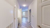 This single-floor unit offers a well-organized layout with a clean, contemporary aesthetic throughout. The entryway hallway features light gray wood-style flooring that extends into the main living areas, creating a cohesive and easy-to-maintain surface underfoot. Flush-mount ceiling lighting and a neutral white and gray color palette lend the interior a bright, open feel.

The kitchen is a functional highlight, equipped with warm honey-toned wood cabinetry, stainless steel appliances including a refrigerator, gas range, and microwave, and a granite-topped peninsula island. Recessed lighting illuminates the space, while a nearby window allows natural light to filter in.

The bedrooms are finished with plush wall-to-wall carpeting and feature windows with blinds that provide natural light and privacy. One bedroom includes a dedicated closet with built-in rod storage, along with access to an additional door, offering practical storage solutions.

The bathroom includes a full tub-shower combination with tiled surround, a wood-toned vanity with a granite countertop, and wood-style flooring consistent with the rest of the unit.

A private balcony extends the living space outdoors, offering views of surrounding trees, landscaped greenery, and the neighboring community streetscape.