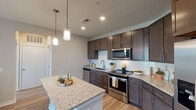 This single-floor residence offers a thoughtfully designed layout with modern finishes throughout. The kitchen serves as a central highlight, featuring rich dark cabinetry that extends to the ceiling, granite countertops, a white subway tile backsplash, and a full suite of stainless steel appliances including a refrigerator with ice maker, electric range, built-in microwave, and dishwasher. A generously sized center island with matching granite provides additional prep space and casual seating, illuminated by two pendant lights overhead. Wood-look flooring flows throughout the kitchen and connects seamlessly to the living areas.

The bedrooms are carpeted for comfort and each feature ceiling fans and windows fitted with horizontal blinds, allowing for natural light and views of the surrounding community and palm trees. The rooms offer ample wall space and a neutral color palette suitable for a variety of furnishing styles.

Two bathrooms serve the residence. One features a dark-cabinet vanity with a white countertop, a large mirror, and wood-look flooring. The second, more spacious bathroom includes a double-sink vanity and a glass-enclosed tiled shower with full-height tile surrounds. Both bathrooms are finished with clean, contemporary hardware and fixtures.