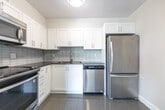 Located at 295 Dufferin St in Toronto's vibrant Dufferin Grove neighbourhood, this single-floor, three-bedroom, one-bathroom unit offers a practical and well-appointed layout. Hardwood-style flooring runs throughout, complemented by neutral walls and textured ceilings that add subtle character to each room. The open living area is bright and airy, with large windows that invite generous natural light and offer views of surrounding greenery. A structural column with integrated HVAC vents divides the living space thoughtfully, adding architectural definition. The kitchen is a standout feature, boasting white shaker-style cabinetry, dark grey countertops, a sleek tiled backsplash with a vertical subway pattern, and stainless steel appliances including a range and over-the-range microwave. The primary bedroom is a comfortable size and includes mirrored sliding closet doors that enhance the sense of space, while the additional bedrooms are well-proportioned with ample natural light. The full bathroom is finished with classic white subway tile surrounding a soaker tub and shower combination, paired with grey floor tile for a clean, timeless look. Clean white panel doors and trim complete the polished, move-in-ready feel of this well-maintained unit.