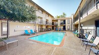 Located in the vibrant Knox-Henderson neighborhood of Dallas, Texas, this courtyard common area at 3516 Matilda St offers a well-appointed outdoor retreat designed for relaxation and community living. The centerpiece of the space is a generously sized swimming pool with clear, blue water, framed by a concrete pool deck finished with terracotta-toned tile edging. Surrounding the pool, a variety of outdoor seating options are thoughtfully arranged, including bright blue lounge chairs, a shaded patio area with a lime-green umbrella and matching accent furniture, and a charming courtyard nook with a seating bench tucked beneath a mature shade tree. A charcoal grill station is conveniently positioned nearby, adding to the outdoor living appeal. The space is enclosed by multi-story residential buildings featuring neutral beige siding, dark-trimmed balconies, and private patios on the ground level separated by black iron railings. Exterior staircases provide access to upper-level units, enhancing the open-air, courtyard-style atmosphere. The mature tree anchoring one corner of the courtyard adds natural character and shade to the overall setting. This outdoor amenity area benefits from open-sky exposure, creating a bright and inviting environment throughout the day.