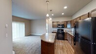 Located at 2829 27th St W in Williston, North Dakota, this single-floor, 3-bedroom, 3-bathroom home offers a well-designed layout with functional living spaces throughout. The open-concept kitchen and dining area is a central highlight, featuring rich dark wood cabinetry, granite-style countertops, black appliances including a range and built-in microwave, a double stainless steel sink, and wood-look flooring. A curved kitchen island with pendant lighting serves as a natural transition into the spacious carpeted living room, which is filled with natural light from a large sliding glass door that opens to an outdoor view. The bedrooms are comfortably sized, each featuring plush carpet flooring, large windows with outdoor views, and baseboard heating. Five closets throughout the home provide ample storage. The three bathrooms are finished with wood-look flooring, dark wood vanities, and granite-style countertops. A dedicated in-unit laundry area accommodates a full-size washer and dryer with overhead shelving for added convenience. Neutral wall tones and consistent finishes carry throughout, giving the home a cohesive and practical aesthetic well-suited for comfortable everyday living.