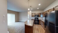 Located at 2829 27th St W in Williston, North Dakota, this single-floor, 3-bedroom, 3-bathroom home offers a well-designed layout with functional living spaces throughout. The open-concept kitchen and dining area is a central highlight, featuring rich dark wood cabinetry, granite-style countertops, black appliances including a range and built-in microwave, a double stainless steel sink, and wood-look flooring. A curved kitchen island with pendant lighting serves as a natural transition into the spacious carpeted living room, which is filled with natural light from a large sliding glass door that opens to an outdoor view. The bedrooms are comfortably sized, each featuring plush carpet flooring, large windows with outdoor views, and baseboard heating. Five closets throughout the home provide ample storage. The three bathrooms are finished with wood-look flooring, dark wood vanities, and granite-style countertops. A dedicated in-unit laundry area accommodates a full-size washer and dryer with overhead shelving for added convenience. Neutral wall tones and consistent finishes carry throughout, giving the home a cohesive and practical aesthetic well-suited for comfortable everyday living.